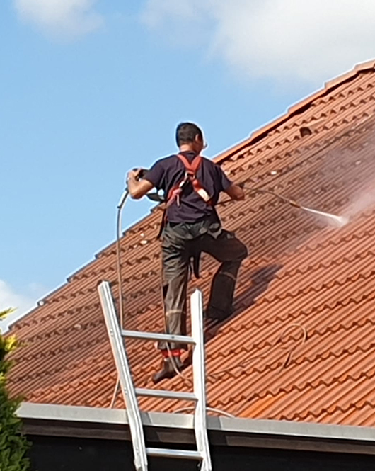 Person wäscht Dach mit Hochdruckreiniger